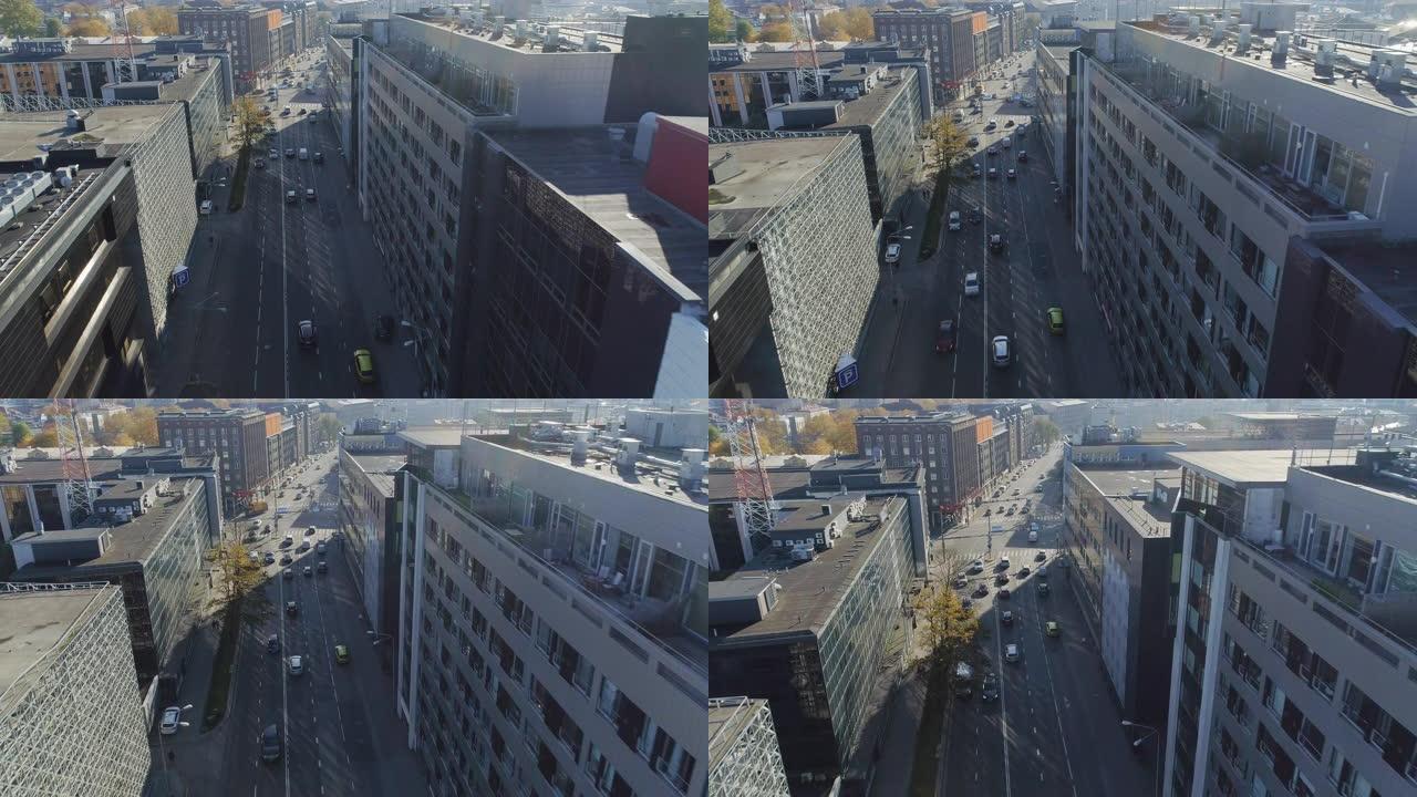 空中无人机镜头在汽车交通适中的城市街道上方飞行。晴天在两排办公楼之间的街道上。