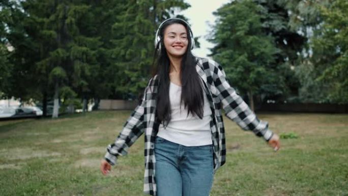 年轻的亚洲女士戴着耳机的慢动作独自在城市公园跳舞