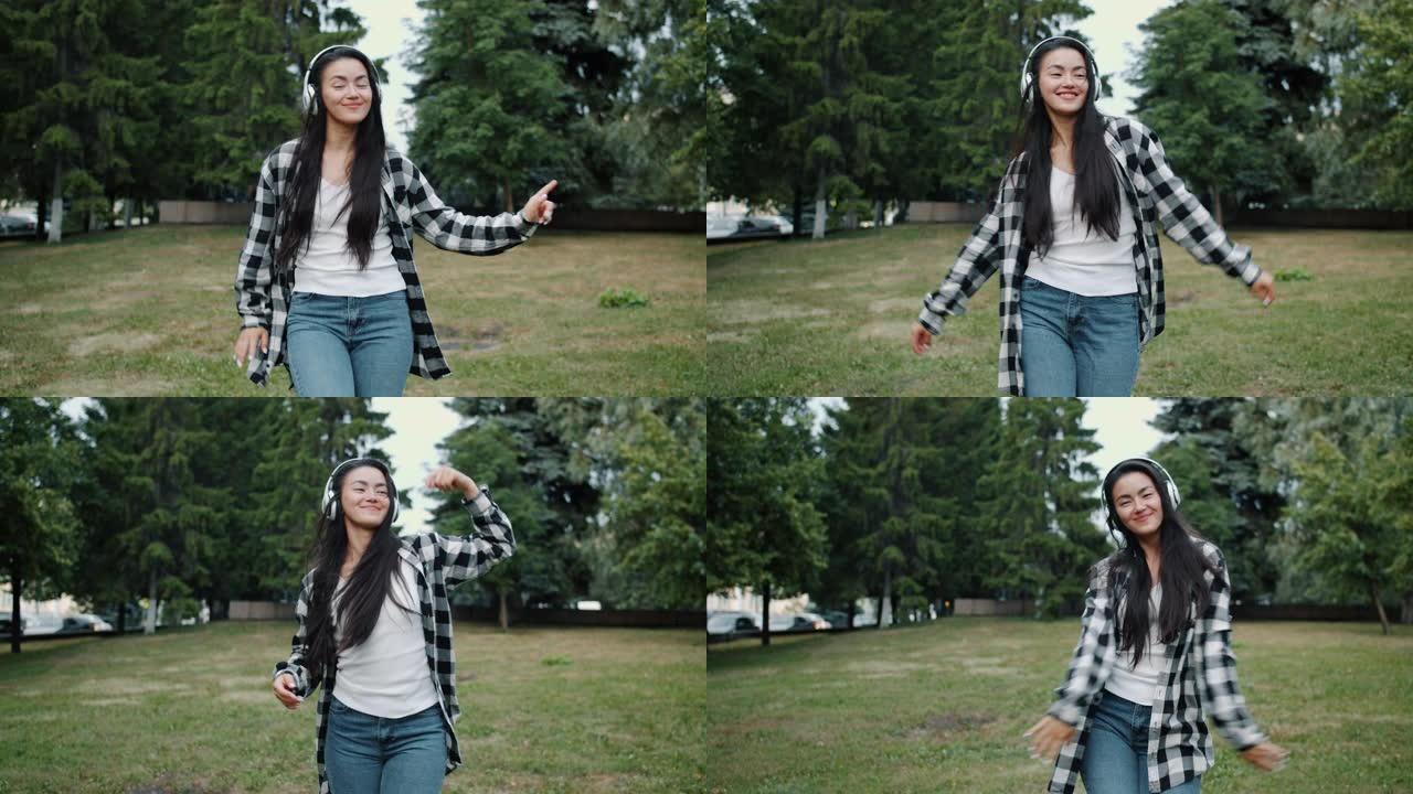 年轻的亚洲女士戴着耳机的慢动作独自在城市公园跳舞