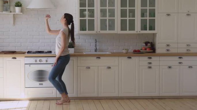有趣的快乐女孩拿着搅拌器麦克风在厨房唱歌跳舞