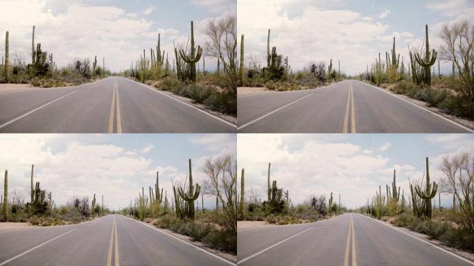 相机在空旷的沙漠道路中间迅速倾斜，大仙人掌在美国亚利桑那州的两侧生长。