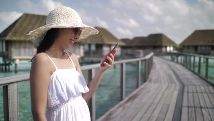 在Maldive海滩使用智能手机上的应用程序发送智能手机短信。亚洲白人妇女在户外使用智能手机