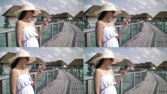 在Maldive海滩使用智能手机上的应用程序发送智能手机短信。亚洲白人妇女在户外使用智能手机