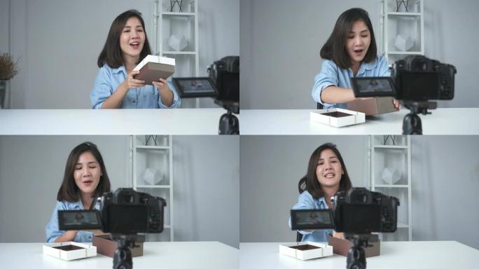 快乐美丽的亚洲女人打开品牌或她的订阅者的礼物。女性博客作者从摄像机录制视频以播放拆箱视频。