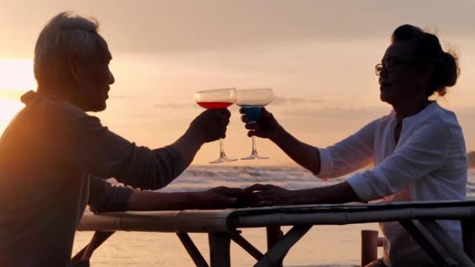 剪影快乐的高级夫妇在日落时野餐和碰杯。浪漫的高级夫妇在暑假。高级夫妇在海边放松。高级假期，假期