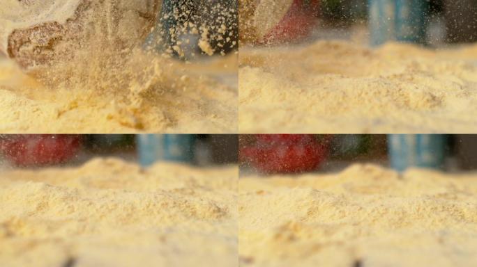 慢动作: 当质朴的面包落在桌子上时，黄色的面粉在空中飞舞。