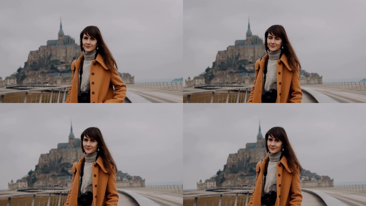 美丽平静的黑发摄影师女人在神奇的圣米歇尔山城堡慢动作对着镜头微笑的肖像