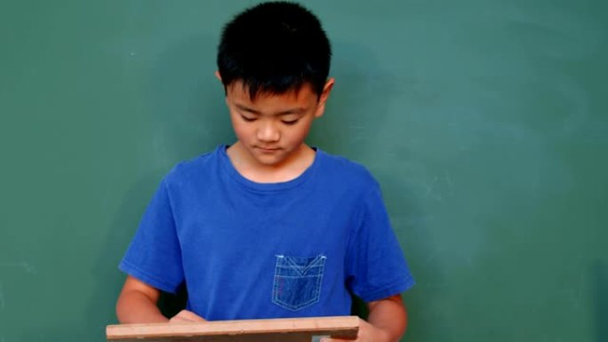4k学校教室里亚洲男生在石板黑板上写作和展示文字的前视图