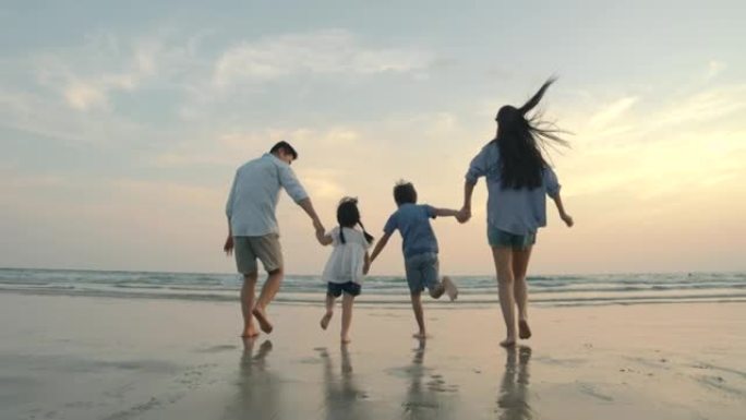 慢动作-亚洲家庭在日落时带着快乐的情感在沙滩上奔跑。家庭、假期和旅行概念。后视图。
