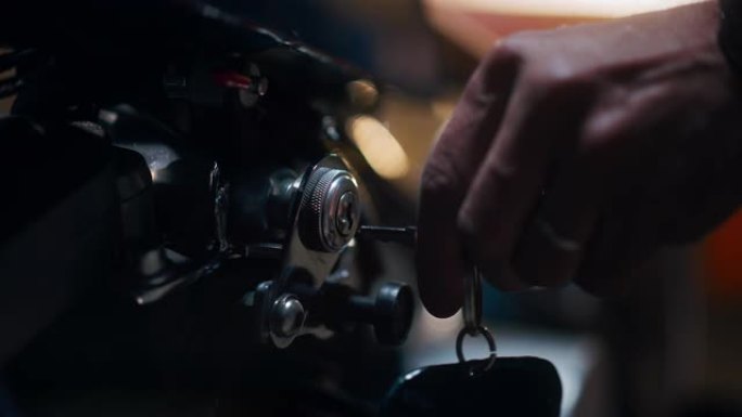 宏关闭了一个人的细节，该人将钥匙放在一个真正的车库中的定制摩托车的点火装置中。他正在转动钥匙并启动马