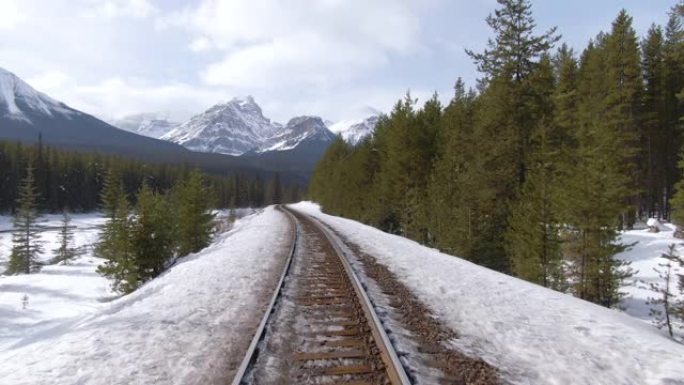 无人机: 沿着生锈的火车轨道飞行，穿过白雪皑皑的松树林。