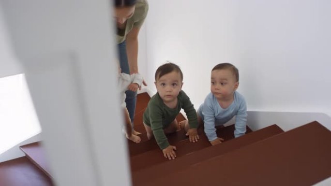 亚洲蹒跚学步的三胞胎爬上楼梯，妈妈帮忙