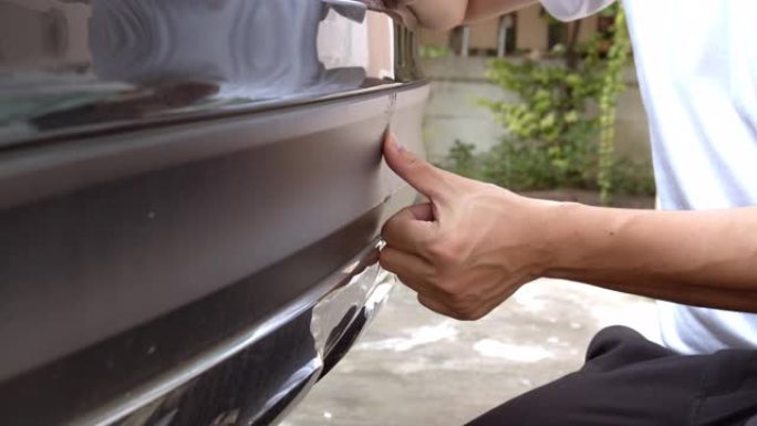 亚洲男子手指指向保险杠上刮伤的汽车。保险概念。