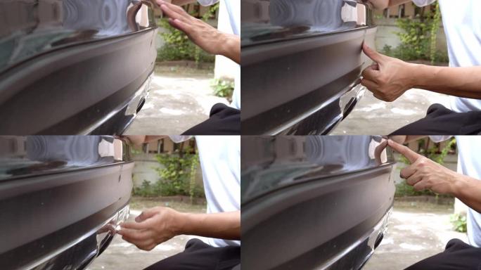 亚洲男子手指指向保险杠上刮伤的汽车。保险概念。