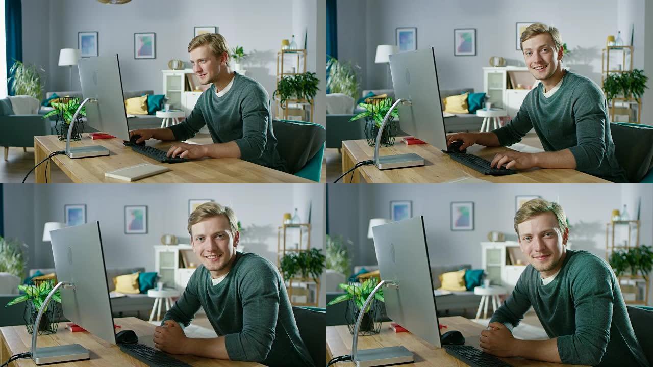 这位专注的年轻人坐在办公桌前，微笑着看着相机，在个人电脑上工作的肖像。背景舒适的客厅。