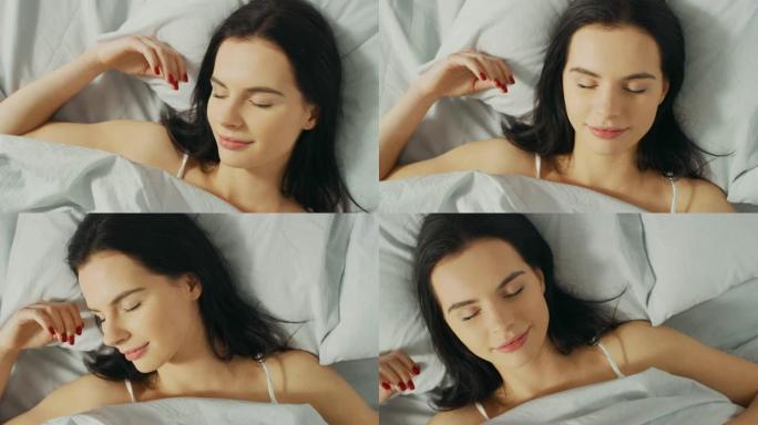 美丽的年轻黑发女人的肖像在清晨迷人地睡在她的床上。安静睡觉的女孩甜美温暖的景色。自上而下的旋转相机拍