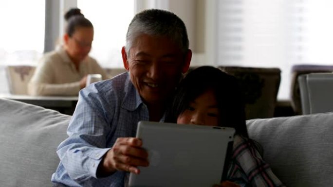 可爱的亚洲孙女和老祖父在家使用数字平板电脑的前视图4k