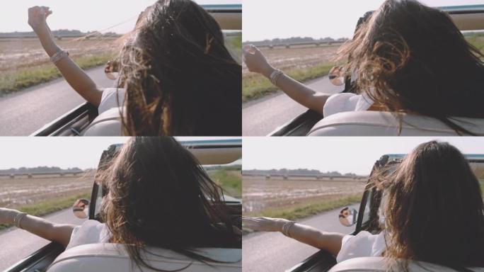 CU SLO MO风吹着无忧无虑的年轻女子的头发，沿着阳光明媚的乡村田野开着敞篷车