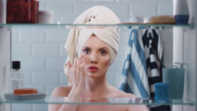 透过浴室柜，可以看到戴着毛巾在头上化妆的女人