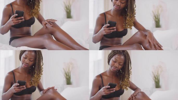 迷人的黑人妇女看着手机并涂上奶油