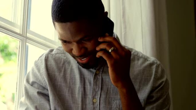 在舒适的家庭中，年轻的黑人男子在手机上聊天的前视图4k