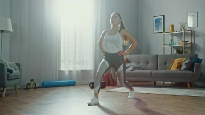穿着运动服的强壮美丽的运动健身女孩正在她明亮宽敞的公寓里做向前的弓步运动，室内简约。