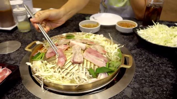 用筷子放在韩国平底锅上的烧烤架。韩国餐馆烤的特写猪肉片。