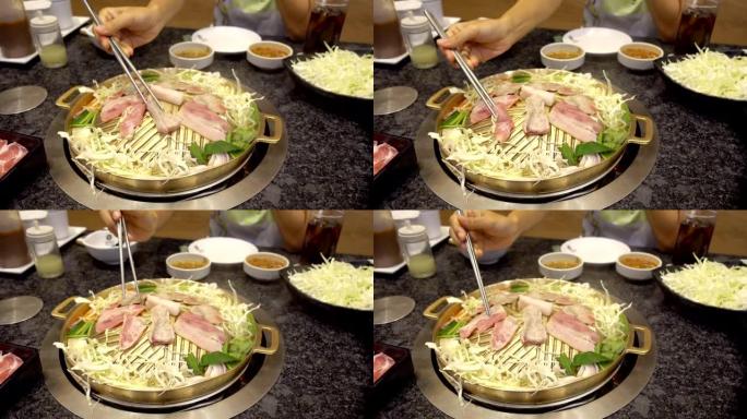 用筷子放在韩国平底锅上的烧烤架。韩国餐馆烤的特写猪肉片。
