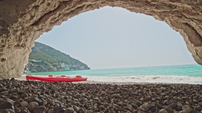 女士在意大利普利亚阳光明媚的偏远海滩上的拱门下的岩石上的皮划艇女士