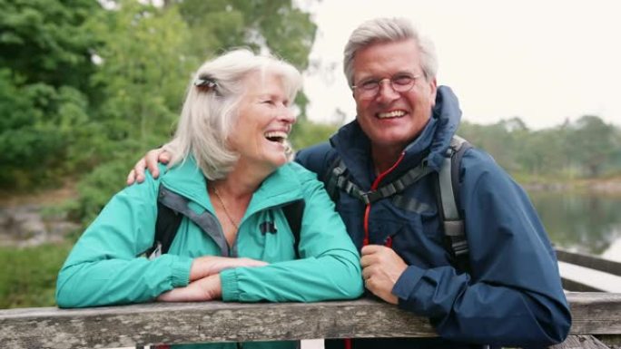 快乐的老年夫妇靠在木栅栏上对着镜头大笑，特写，英国湖区