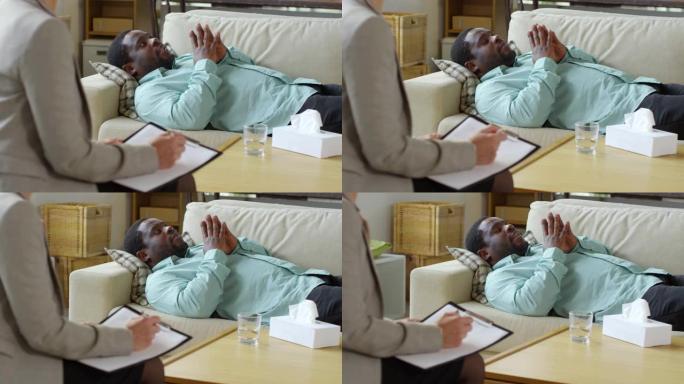 非洲男性患者躺在沙发上与女心理学家交谈