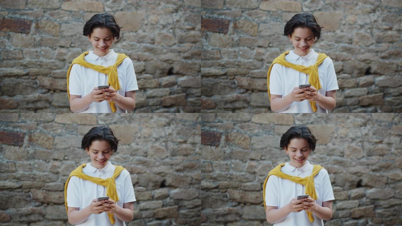 快乐的十几岁的男孩在街上使用智能手机微笑着玩小工具