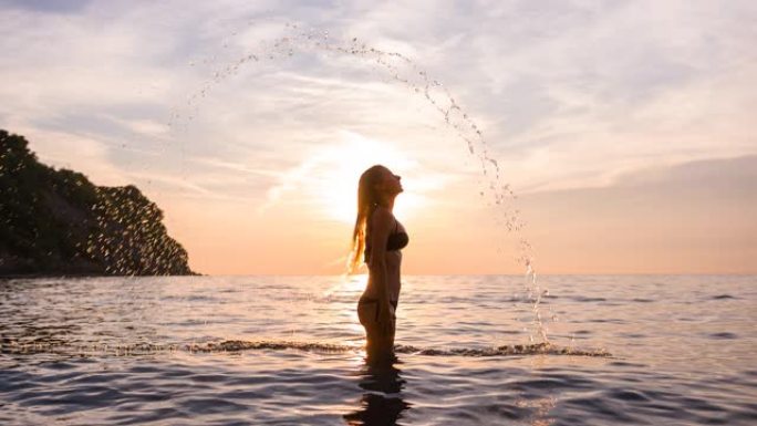 享受夏天的女人，在日落时把长长的湿头发扔回海里，水滴掉下来