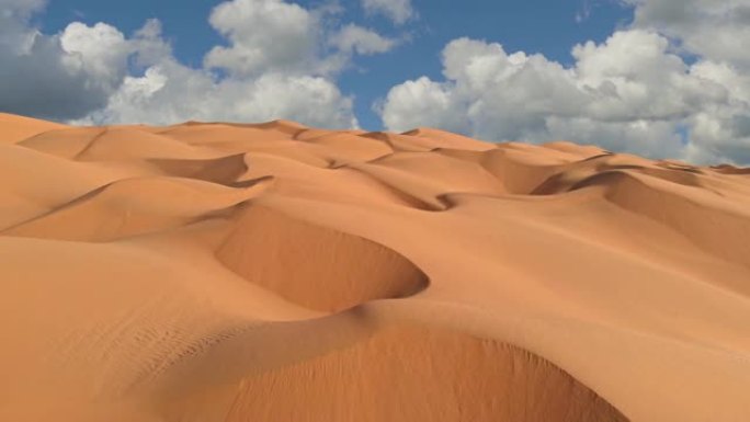 飞越沙漠中无尽的黄色沙丘。沙丘和云密布的蓝天。UHD美丽的沙漠景观鸟瞰图