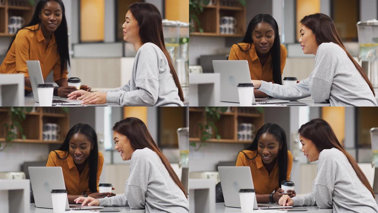 两名在现代办公室厨房区域使用笔记本电脑的女商人