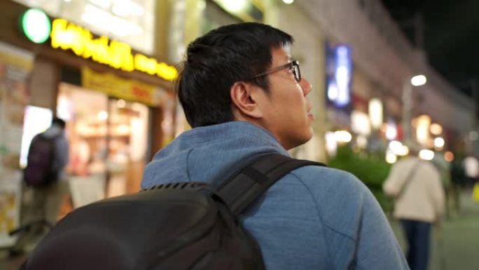 亚洲游客走着走着，寻找日本东京夜生活街的灵感的后视图