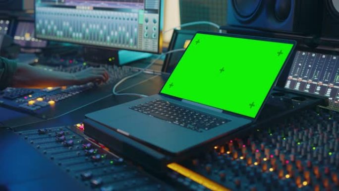 现代音乐录音室控制台，配有绿屏色度键笔记本电脑、均衡器、混音器和其他专业设备。切换器、按钮、推子、滑