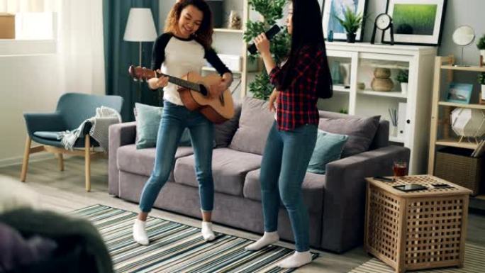 可爱的年轻女士亚洲和非裔美国人正在用遥控器唱歌，在家里弹吉他放松，表达积极的情绪。友谊和有趣的概念。