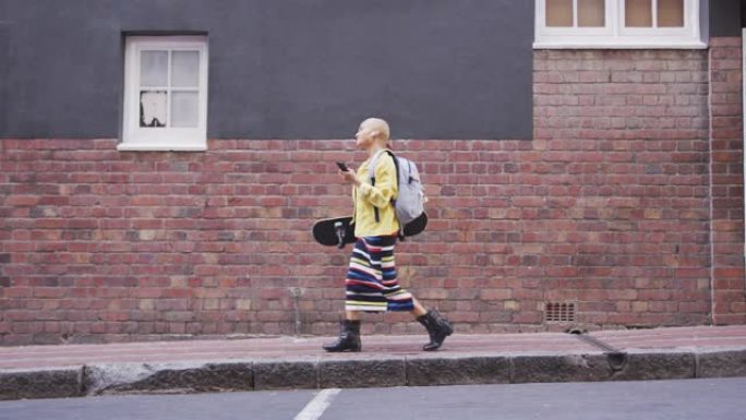 混血女人拿着滑板和手机走在街上