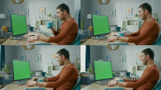 坐在家里办公桌前的英俊男人使用带有绿屏模型的个人计算机。他喝杯子里的饮料。
