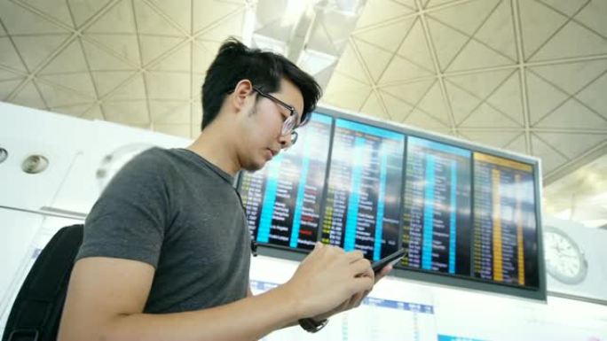 亚洲男子在机场看出发飞机和智能手机