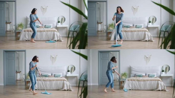 快乐的年轻女士用拖把洗地板，在卧室里在家跳舞