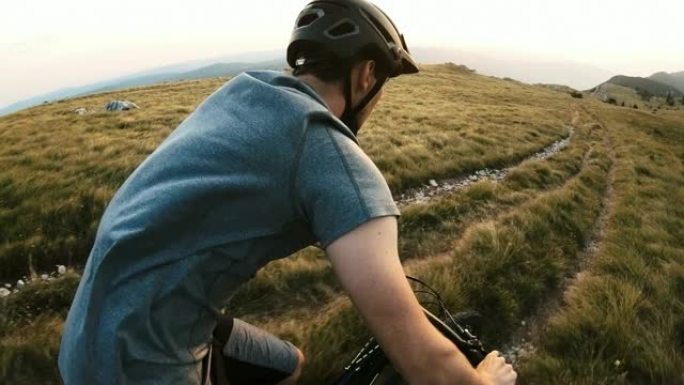 在阳光明媚的日子里，男子在高山上绿草如茵的自行车道上骑自行车