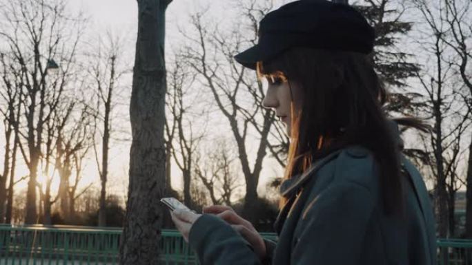 电影侧视图，美丽的女人沿着日落秋公园散步使用智能手机购物应用程序微笑慢动作。