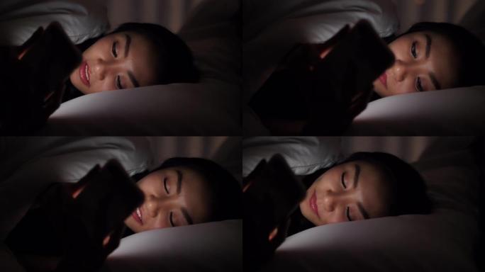 美丽的女人躺在床上，晚上使用智能手机