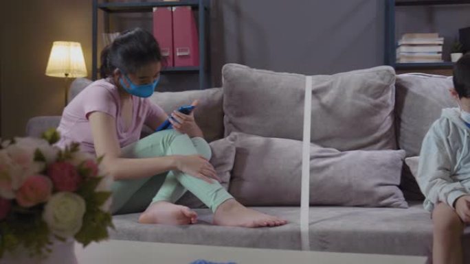 两个亚洲姐姐在客厅里玩智能手机，在家里的沙发中间用胶带粘了一条线。减少细菌传播概念