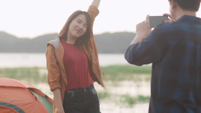 年轻的亚洲夫妇使用智能手机在海滩附近互相拍照。