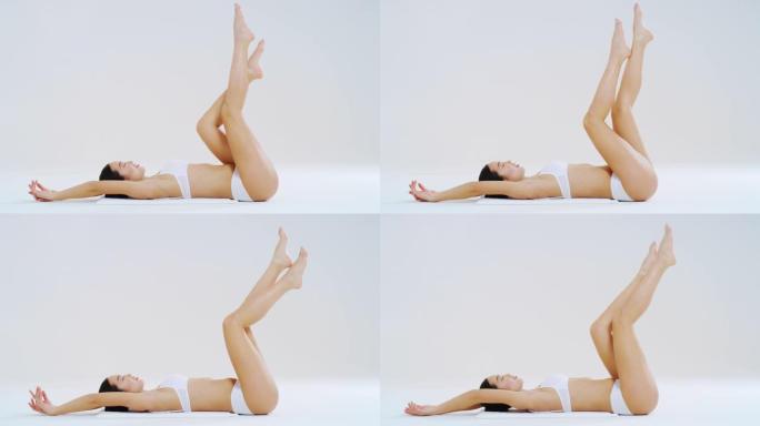 年轻的亚洲女性的慢动作，完美的身体躺在地板上，在脱毛后露出无毛柔软柔滑的双腿，孤立在白色背景上