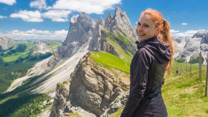 年轻的女徒步旅行者从意大利多洛米蒂的塞塞达山顶欣赏壮丽的景色，对着镜头微笑