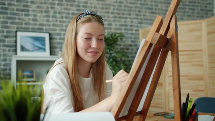 快乐的年轻女士在家用彩色铅笔坐在画架上画画